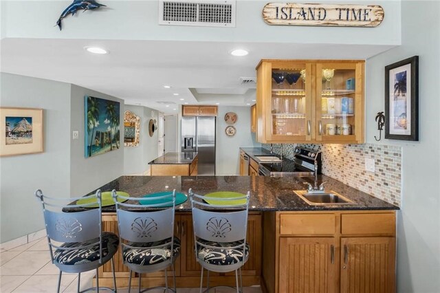 kitchen with appliances with stainless steel finishes, sink, a breakfast bar area, backsplash, and dark stone counters