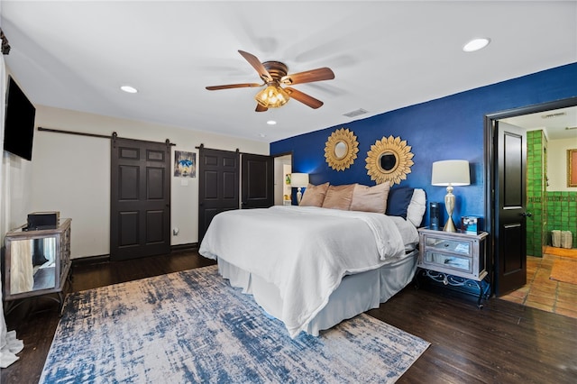 bedroom with a barn door, ceiling fan, and dark wood-type flooring