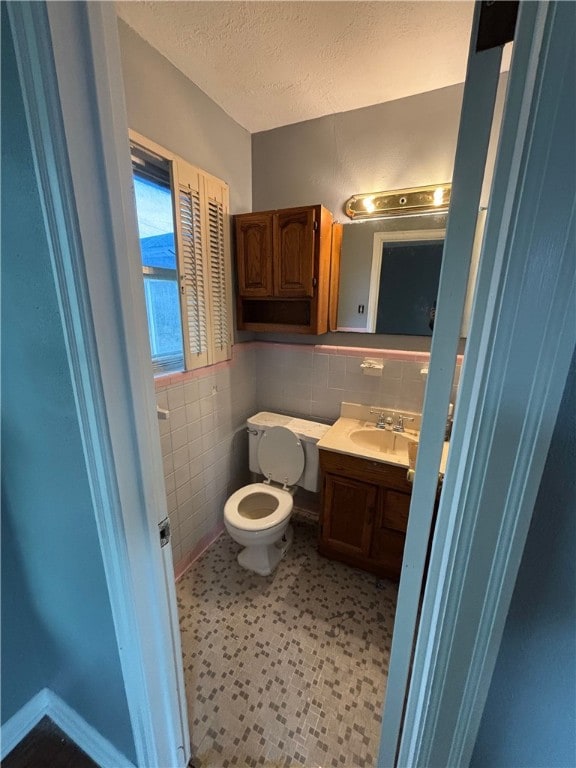 bathroom with a textured ceiling, vanity, toilet, and tile walls