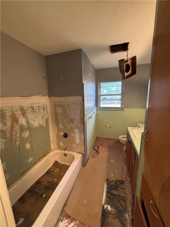 bathroom with a washtub, vanity, a textured ceiling, and toilet