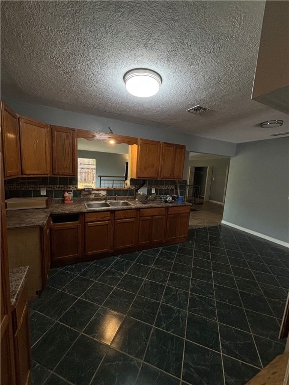 kitchen with a textured ceiling, backsplash, dark tile patterned floors, and sink