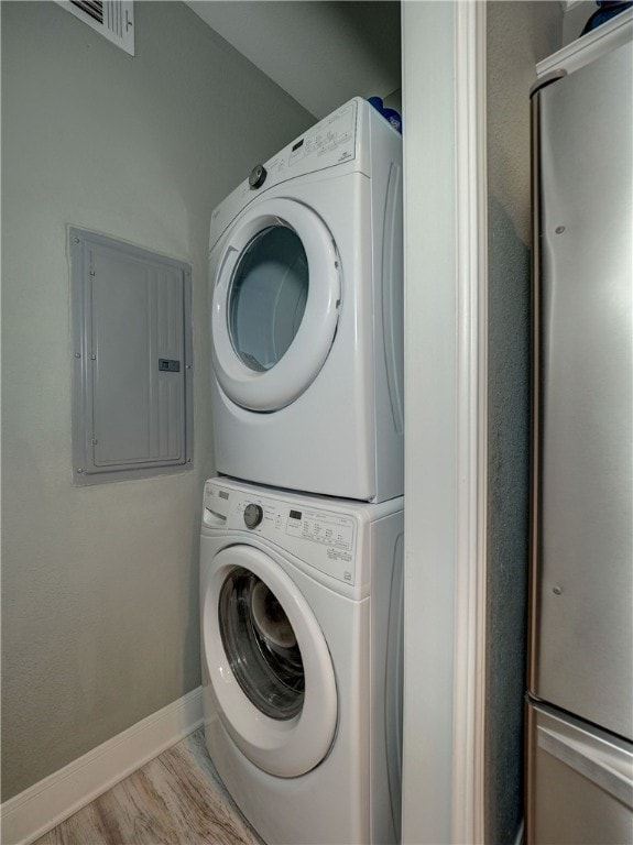 laundry room featuring stacked washing maching and dryer, electric panel, and light hardwood / wood-style floors