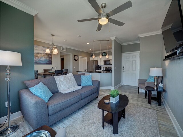 living room with ceiling fan with notable chandelier, light hardwood / wood-style floors, and crown molding