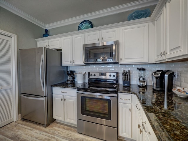 kitchen with dark stone counters, white cabinets, crown molding, light wood-type flooring, and appliances with stainless steel finishes