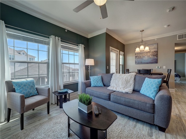 living room featuring light wood-type flooring, ceiling fan with notable chandelier, a healthy amount of sunlight, and crown molding