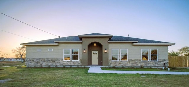 view of front of house with stone siding, a front yard, and fence