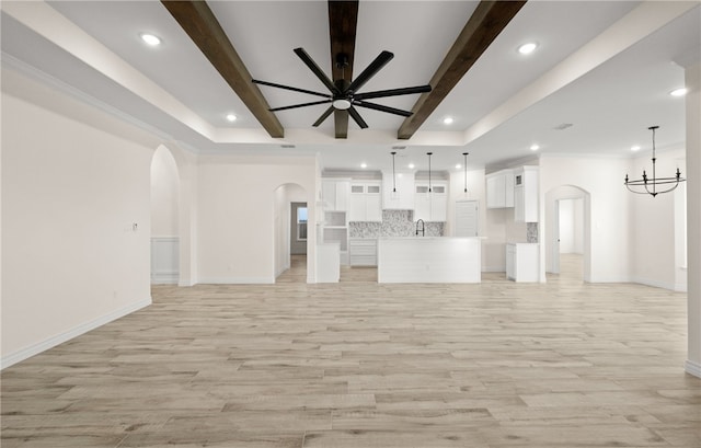 unfurnished living room featuring ceiling fan with notable chandelier, beam ceiling, light wood-type flooring, and sink