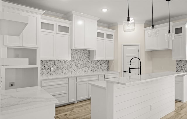 kitchen with white cabinetry, sink, hanging light fixtures, light hardwood / wood-style floors, and a kitchen island with sink