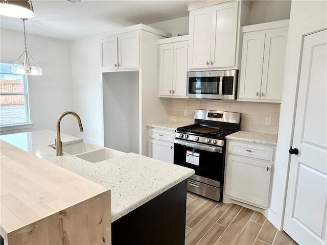 kitchen featuring a kitchen island with sink, wood finish floors, a sink, appliances with stainless steel finishes, and tasteful backsplash