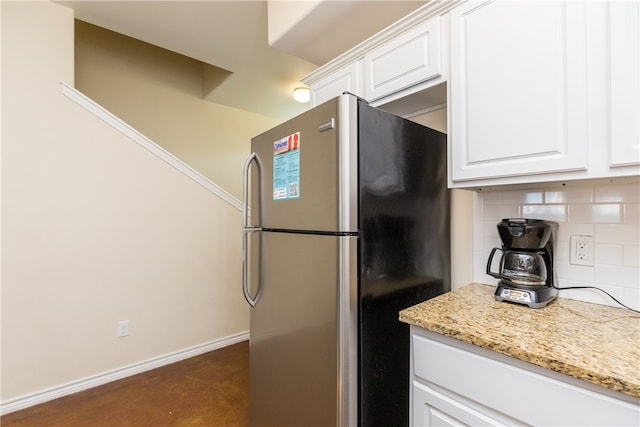 kitchen with white cabinets, stainless steel fridge, backsplash, and light stone counters