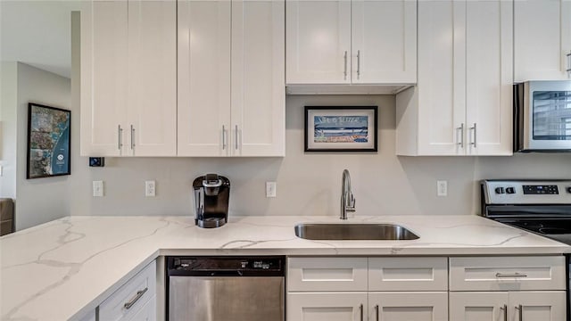 kitchen with stainless steel appliances, white cabinetry, a sink, and light stone countertops