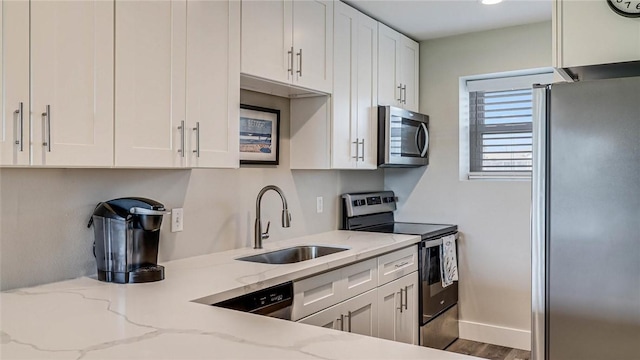 kitchen with white cabinets, light stone counters, wood finished floors, stainless steel appliances, and a sink