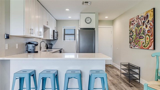 kitchen with visible vents, appliances with stainless steel finishes, white cabinets, a sink, and a peninsula