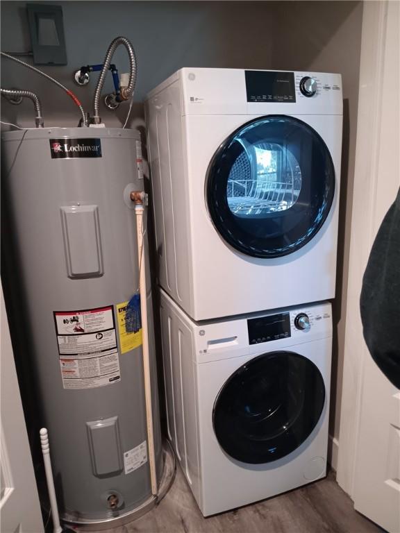 clothes washing area with water heater, wood finished floors, and stacked washer and clothes dryer