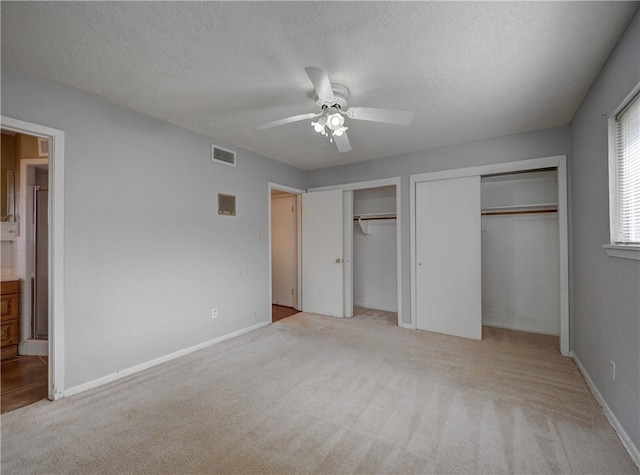 unfurnished bedroom featuring connected bathroom, a textured ceiling, multiple closets, light colored carpet, and ceiling fan