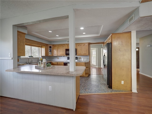 kitchen with dark wood-type flooring, kitchen peninsula, black appliances, a textured ceiling, and a tray ceiling