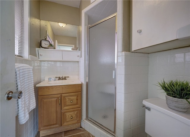 bathroom with walk in shower, vanity, tile patterned floors, toilet, and tile walls