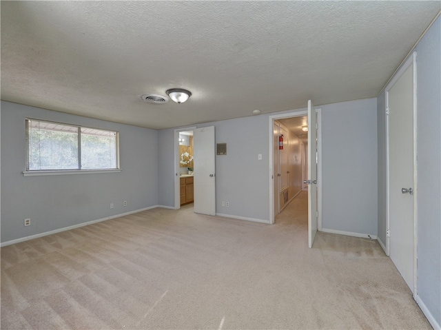 unfurnished bedroom featuring light colored carpet, a textured ceiling, and connected bathroom