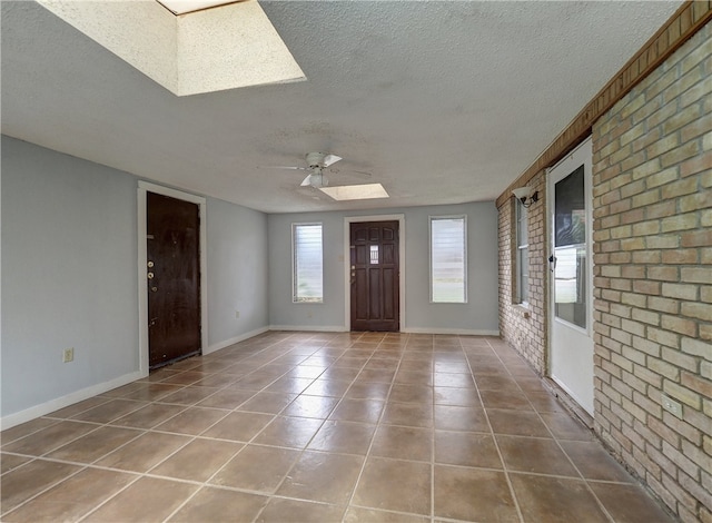 foyer entrance featuring tile patterned flooring, a textured ceiling, ceiling fan, a skylight, and brick wall