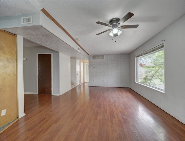 empty room with hardwood / wood-style floors, brick wall, a textured ceiling, and ceiling fan