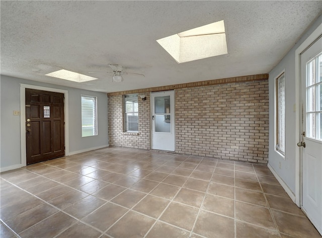 interior space featuring a wealth of natural light, a skylight, ceiling fan, and brick wall