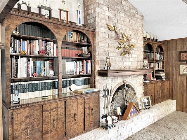interior space with carpet flooring, a textured ceiling, wood walls, a large fireplace, and built in shelves