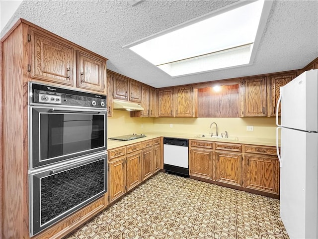 kitchen featuring a textured ceiling, a sink, light countertops, under cabinet range hood, and white appliances