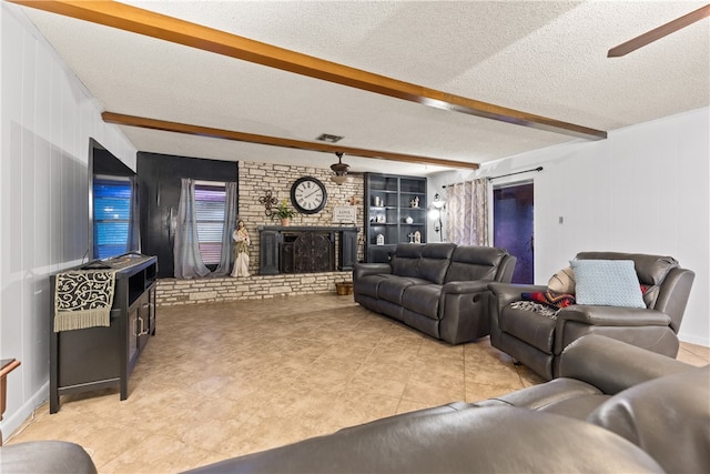 tiled living room with ceiling fan, a textured ceiling, a brick fireplace, and beam ceiling