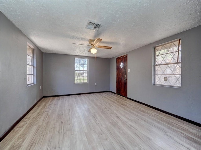 empty room with visible vents, a textured ceiling, light wood finished floors, baseboards, and ceiling fan