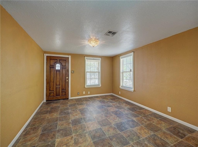 foyer with stone finish flooring, baseboards, visible vents, and a textured ceiling