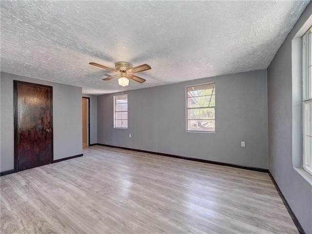 unfurnished bedroom featuring multiple windows, baseboards, light wood finished floors, and a textured ceiling