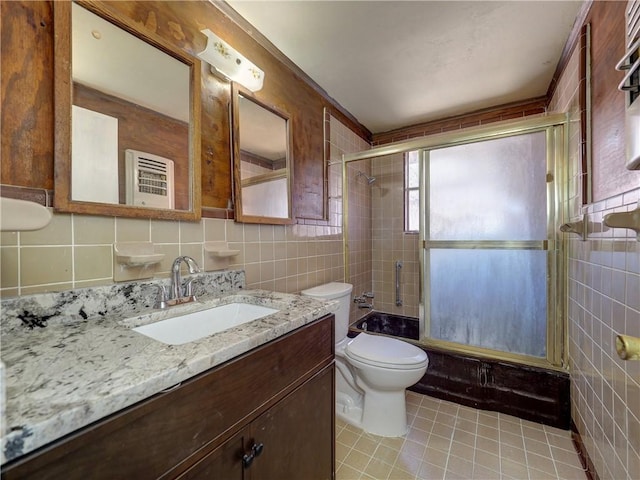 bathroom with tile patterned floors, toilet, tile walls, bath / shower combo with glass door, and vanity