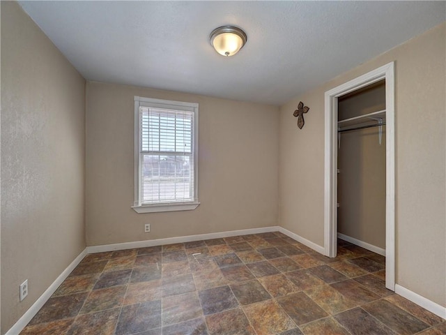 unfurnished bedroom featuring a closet, stone finish floor, and baseboards