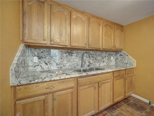 kitchen featuring stone tile floors, decorative backsplash, light stone countertops, and a sink