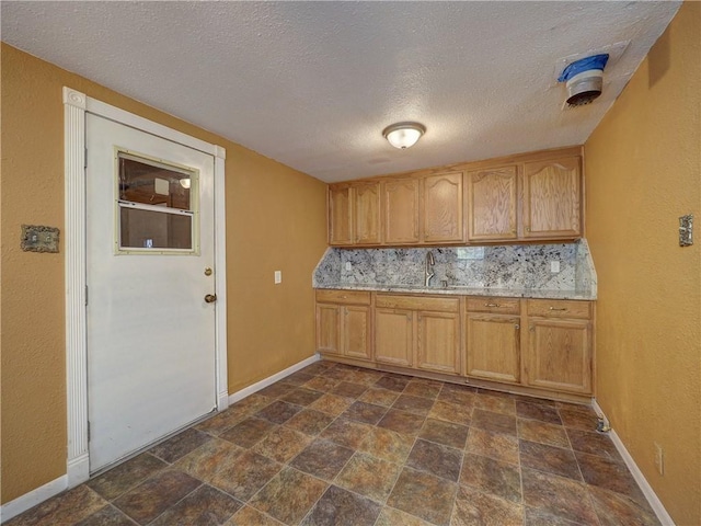 kitchen featuring stone finish floor, a sink, backsplash, light countertops, and baseboards