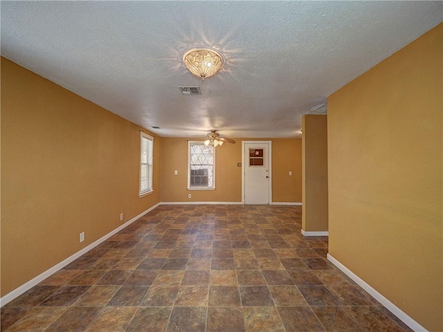 unfurnished room featuring visible vents, baseboards, a textured ceiling, and stone finish floor