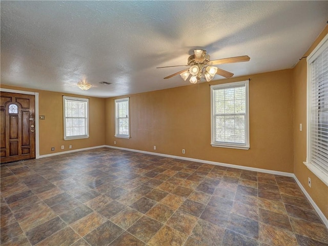 interior space featuring a ceiling fan, visible vents, baseboards, stone finish floor, and a textured ceiling