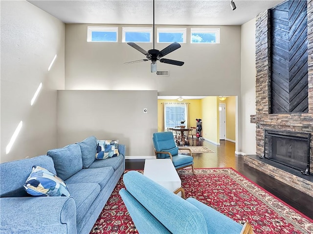 living room with dark wood-type flooring, a fireplace, a high ceiling, and ceiling fan