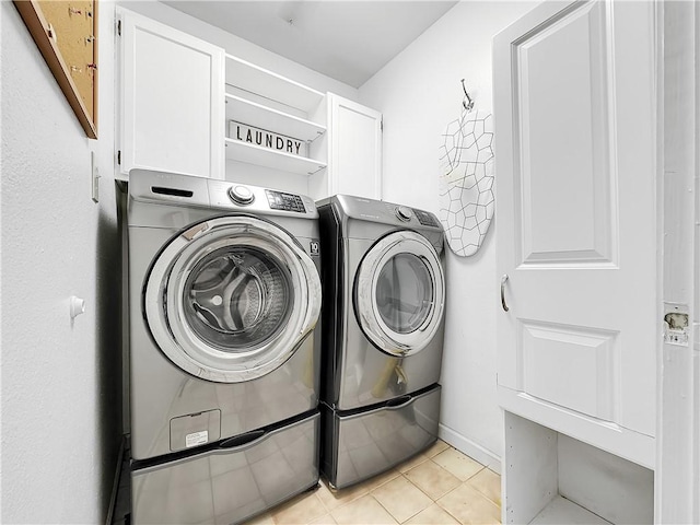 clothes washing area with washing machine and clothes dryer, cabinets, and light tile patterned flooring