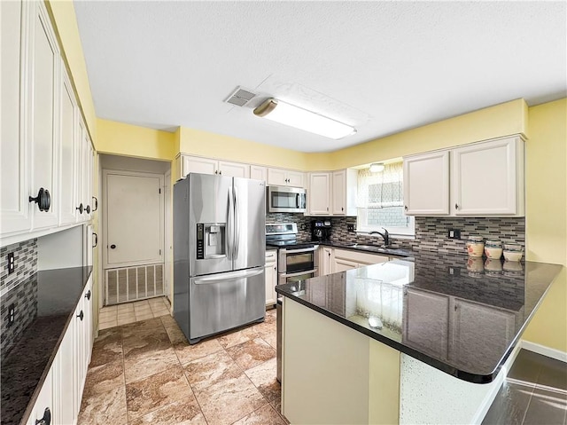 kitchen with white cabinetry, stainless steel appliances, dark stone counters, sink, and kitchen peninsula