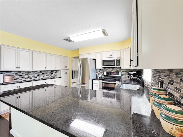 kitchen featuring appliances with stainless steel finishes, white cabinetry, dark stone counters, and sink