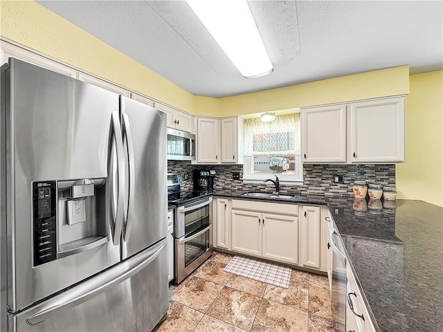 kitchen featuring appliances with stainless steel finishes, white cabinetry, dark stone countertops, sink, and backsplash