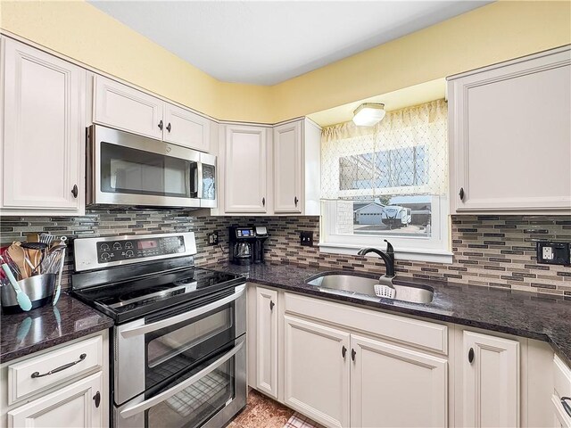 kitchen with appliances with stainless steel finishes, dark stone countertops, white cabinetry, and sink