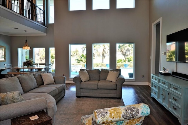 living room featuring a high ceiling, plenty of natural light, baseboards, and dark wood-style flooring