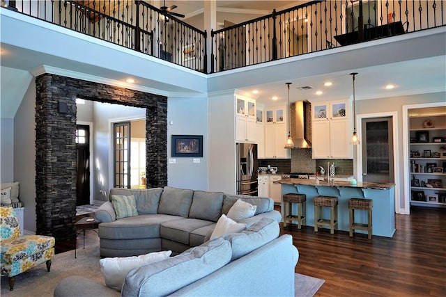 living area with dark wood-type flooring, ornamental molding, a towering ceiling, and ornate columns