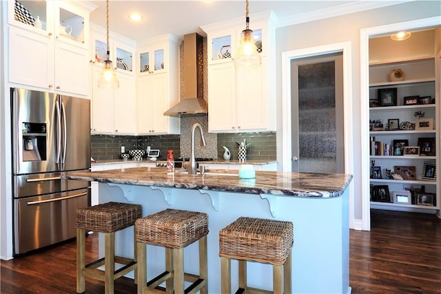 kitchen featuring ornamental molding, stainless steel refrigerator with ice dispenser, dark stone counters, wall chimney range hood, and dark wood-style flooring