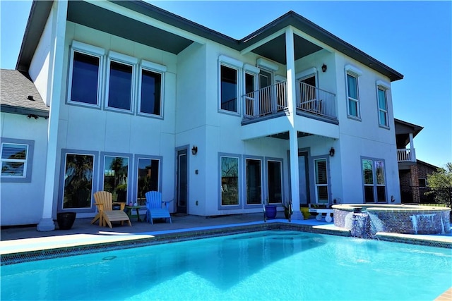 rear view of house with an in ground hot tub, an outdoor pool, and stucco siding