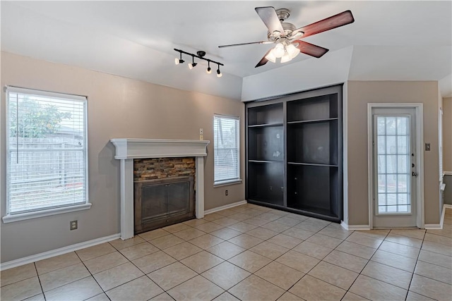 unfurnished living room featuring a healthy amount of sunlight, light tile patterned floors, vaulted ceiling, and a stone fireplace