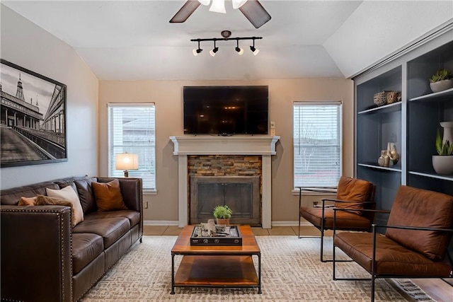 living area with built in features, baseboards, lofted ceiling, ceiling fan, and a stone fireplace