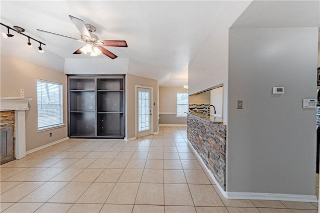 unfurnished living room with a ceiling fan, a healthy amount of sunlight, a stone fireplace, and light tile patterned floors